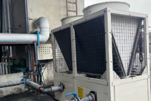 Air-cooled industrial process chiller installed with chilled-water piping at a factory.