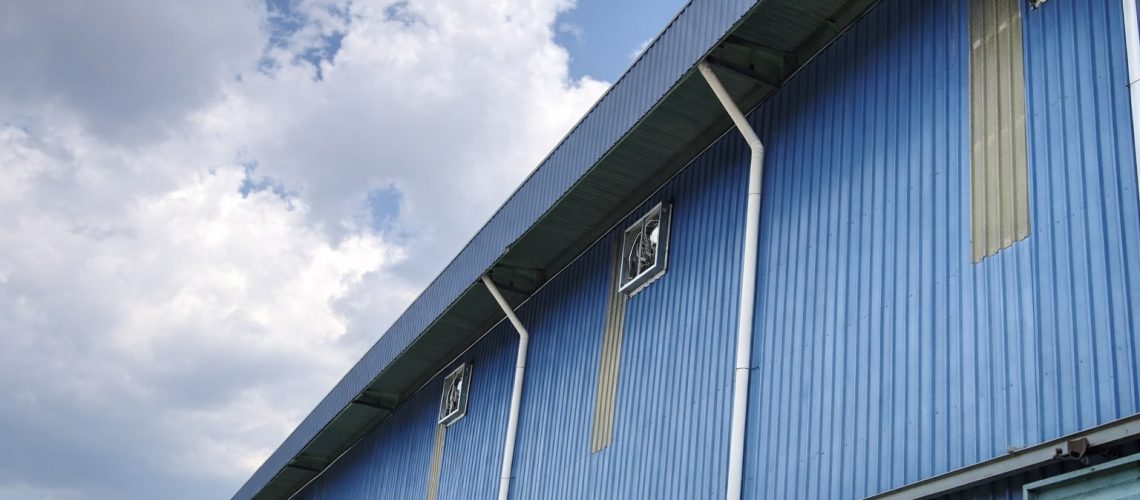 External view of a blue industrial factory featuring multiple CrystalAir box-type exhaust fans installed for active ventilation.