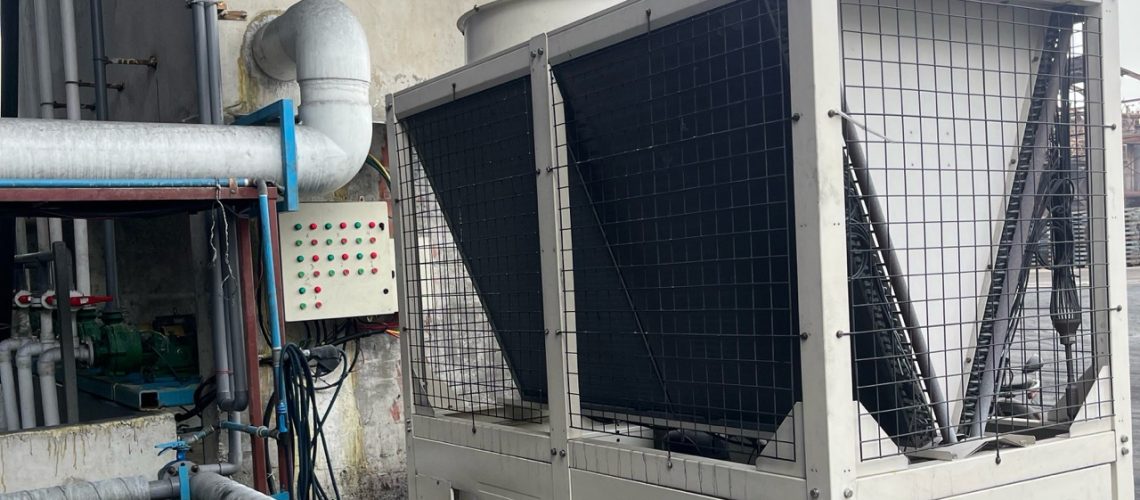 Air-cooled industrial process chiller installed with chilled-water piping at a factory.